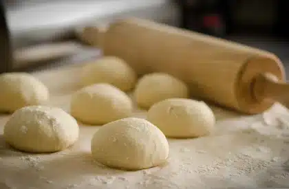 Hands dusting a cloth-lined basket next to a freshly baked loaf, flour dusting visible