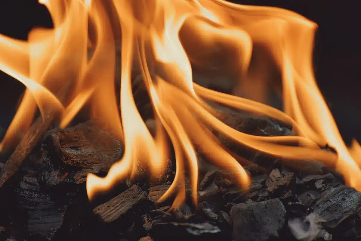 Close-up of meat sizzling on a hot grill with flames and smoke rising