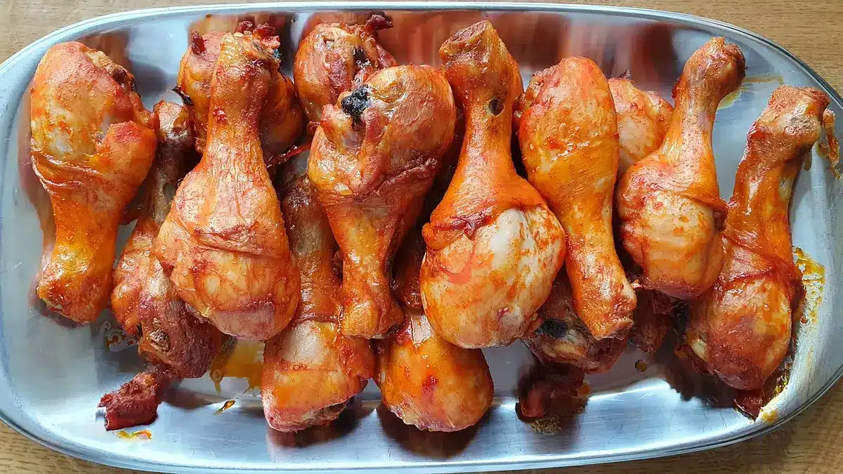 Sealed tray of raw chicken pieces thawing in a refrigerator on the bottom shelf with a catch dish underneath.