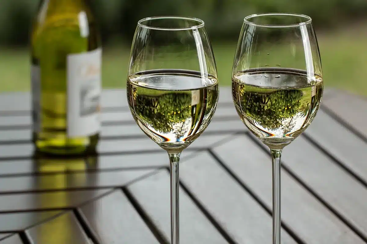 Deux verres de vin blanc côte à côte : un sauvignon blanc pâle et un moscato doré, avec des fruits et des herbes fraîche