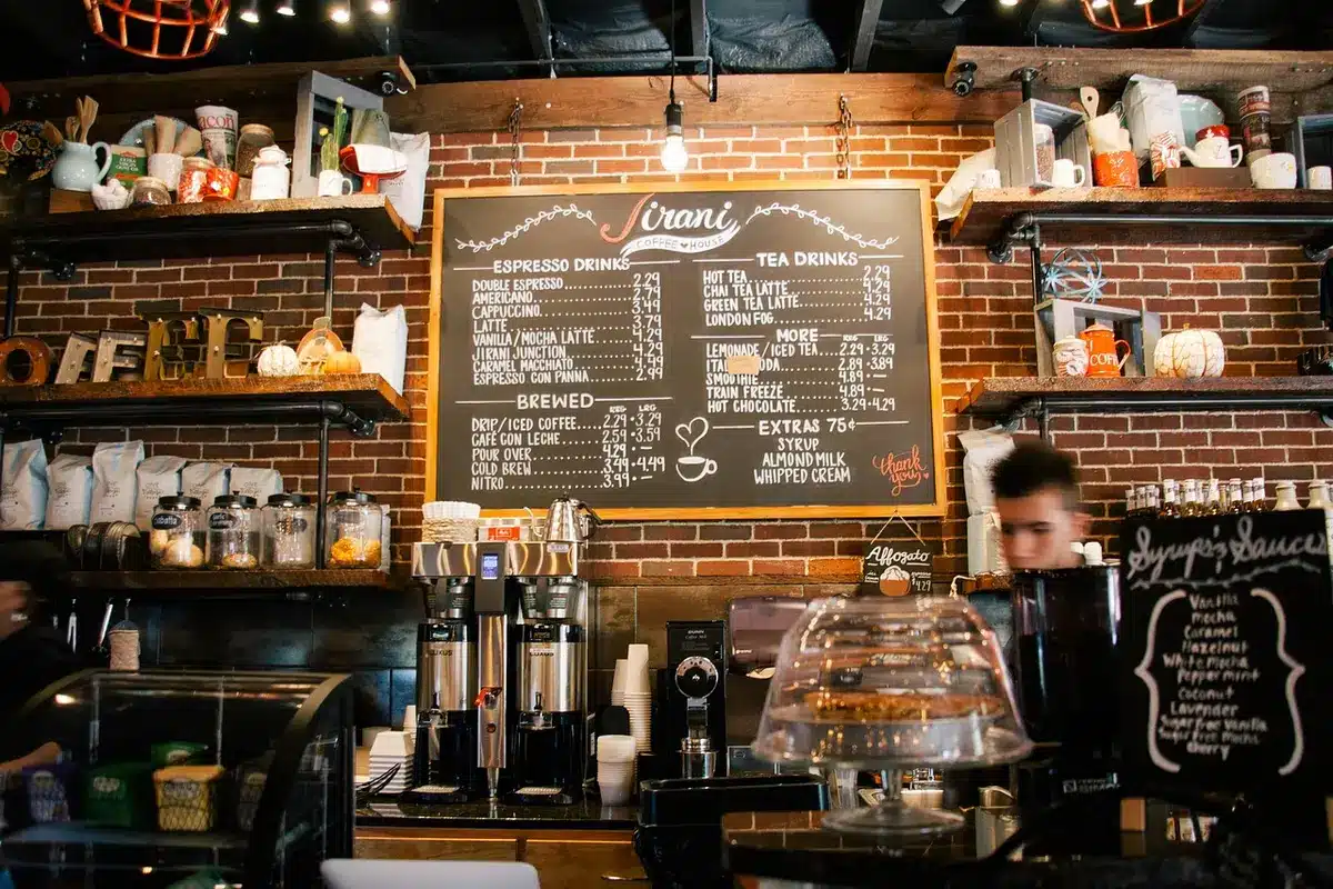 Barista hands pouring colored syrup into an iced coffee drink at a café counter.