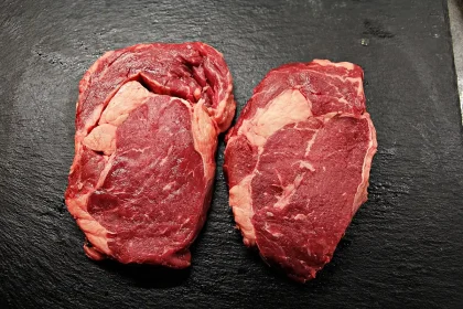 Raw steak on a cutting board with tenderizing tools and ingredients nearby