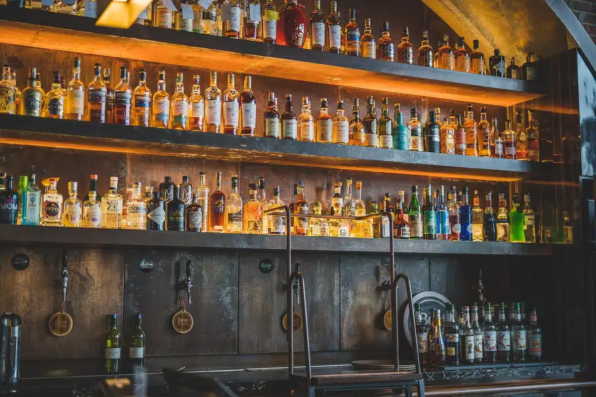 A hand holding a bottle of tequila next to a glass on a bar counter