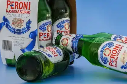 Hands reaching for a beer can and a brown bottle on a picnic table