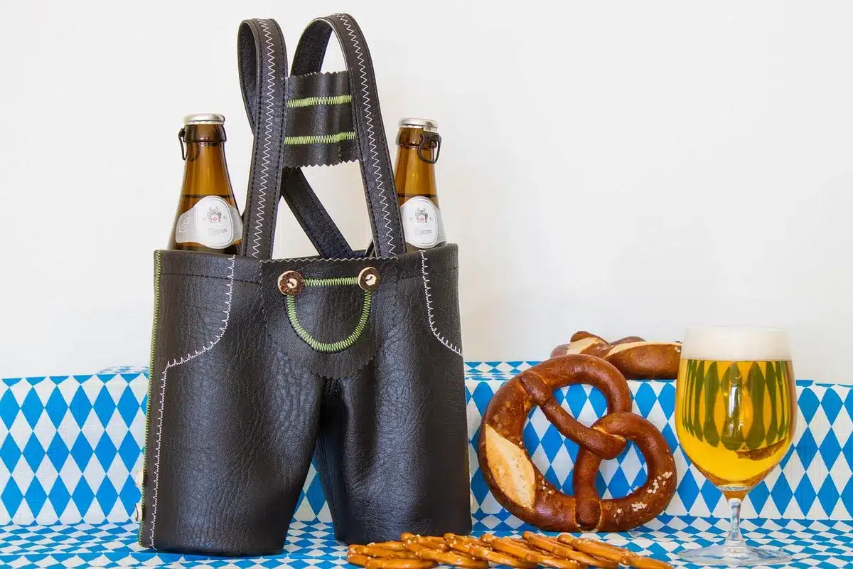 Hands reaching into a cooler for green-bottled six-packs beside a grill in a backyard