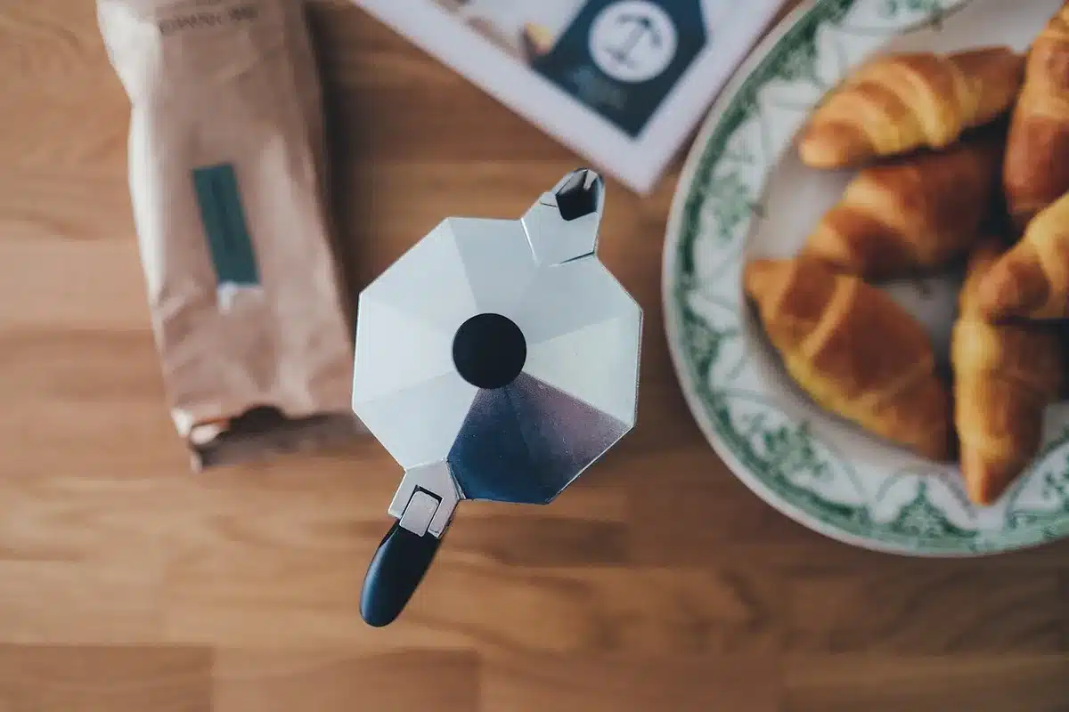 Stainless steel moka pot on an induction cooktop with adapter plate nearby
