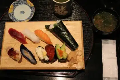 Sunlit wood sushi counter with chef hands arranging nigiri and fresh wasabi